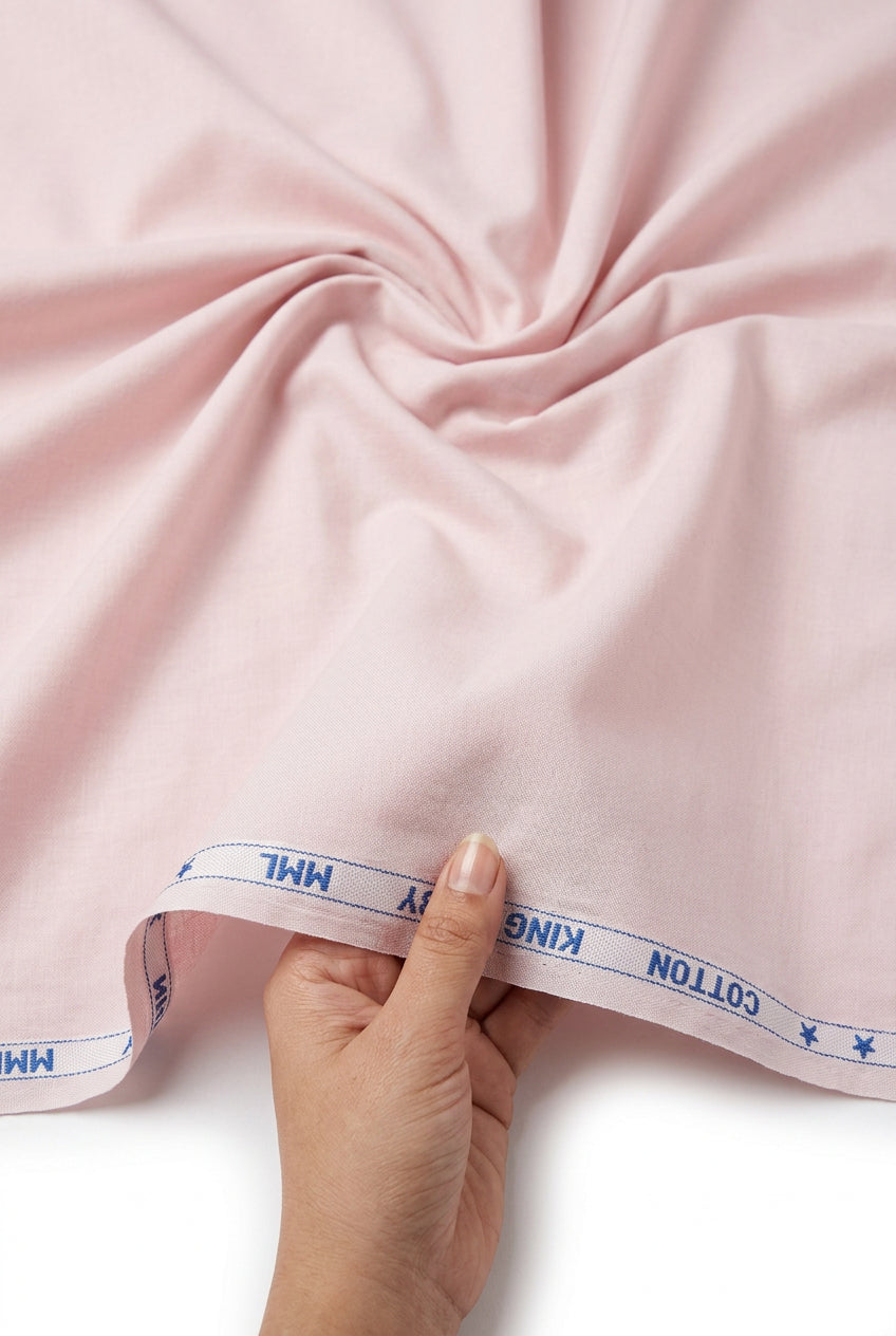 A light pink cotton fabric sheet with visible wrinkles, showing a blue printed edge with 'COTTON' text at the bottom.